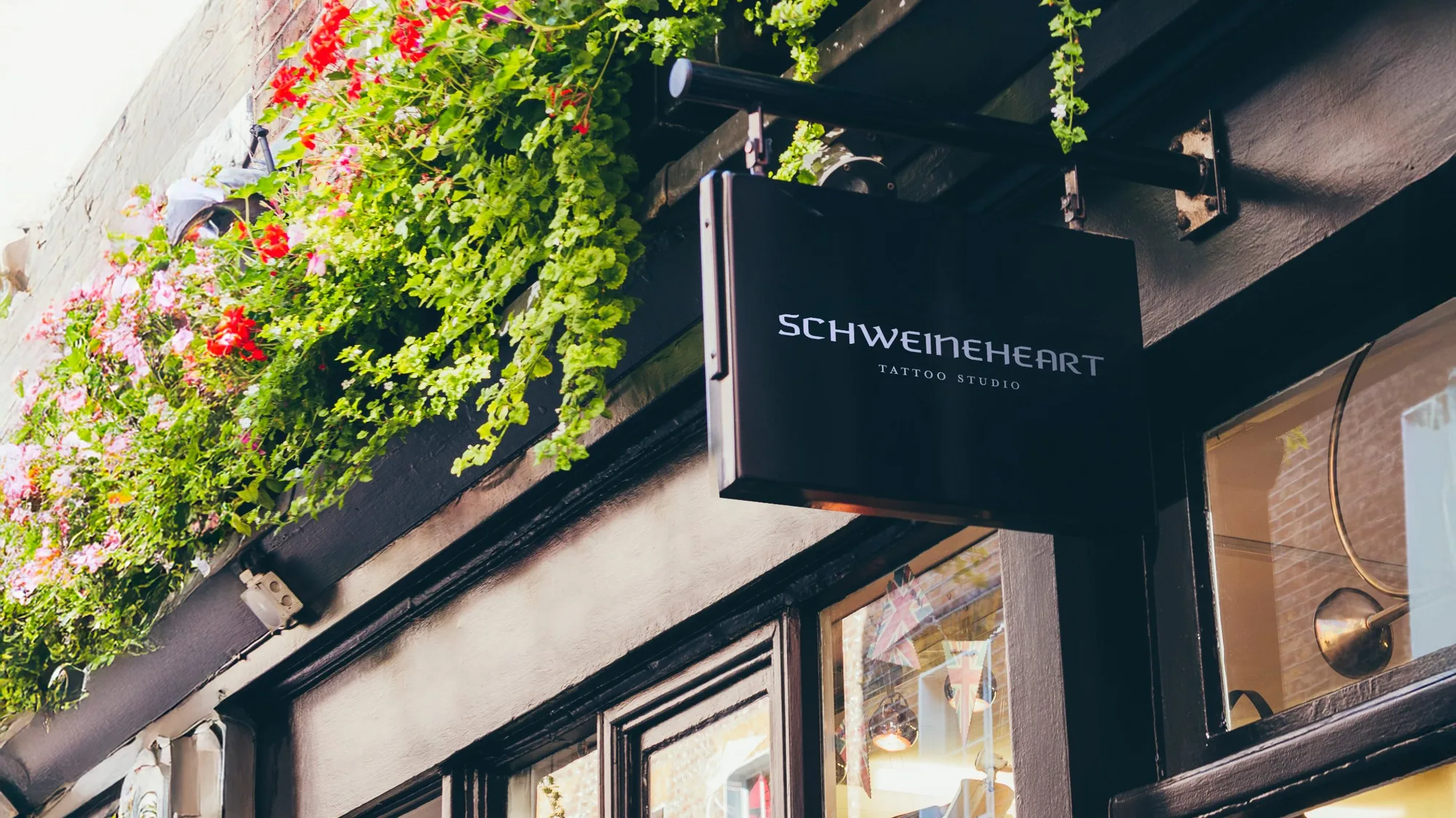 Hanging Schweineheart Tattoo Studio sign under flower boxes on a dark shopfront