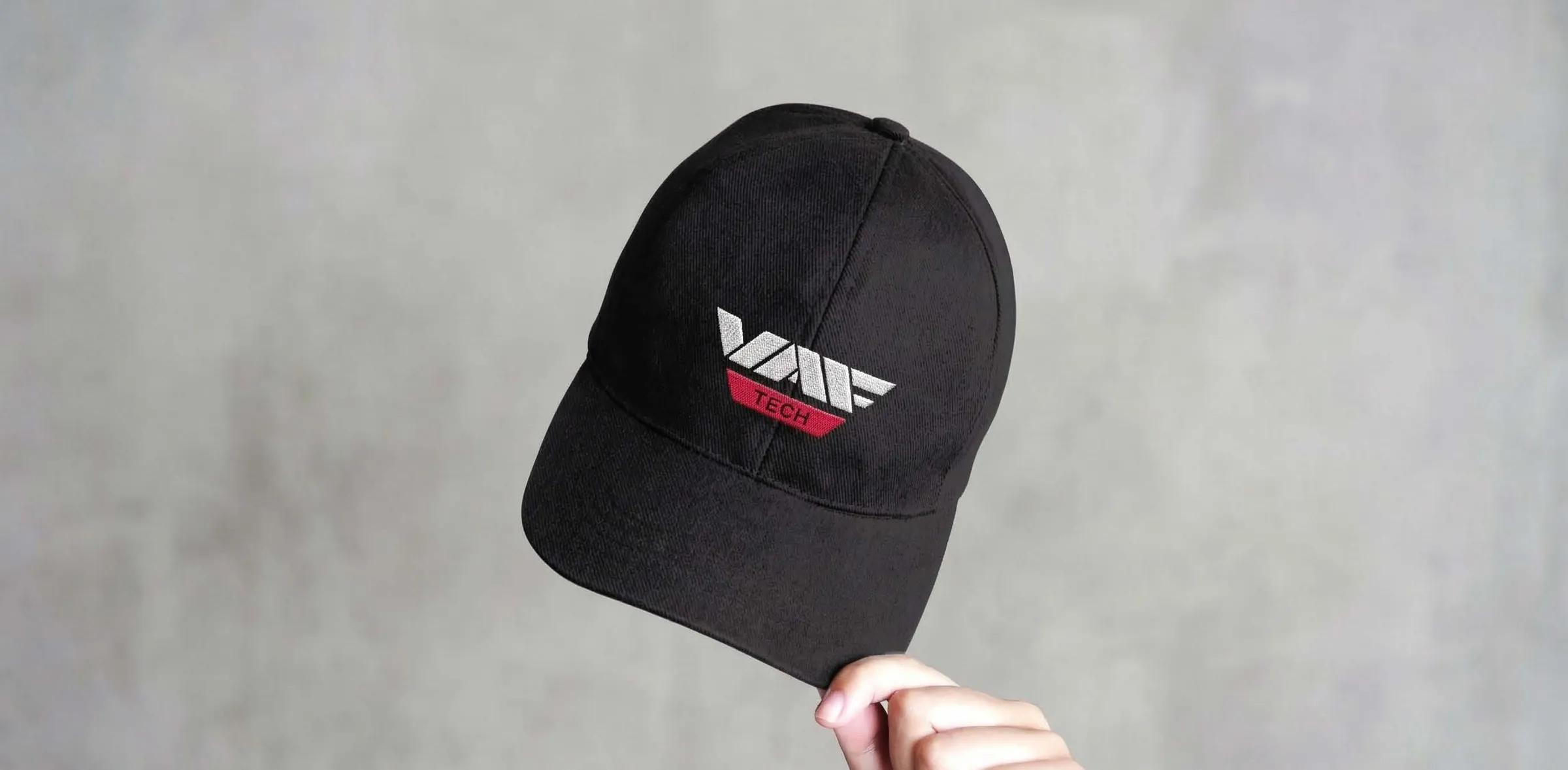 A hand holding a black cap with the magenta VAF Tech logo